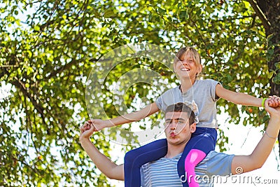 Defocused brother riding sister on back. Portrait of happy girl on man shoulders, piggyback. Girl fly, raise hand Stock Photo