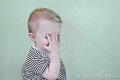 Defocused funny, happy child smiles and covers his face with his hand. The little child is embarrassed. Copy space - Stock Photo