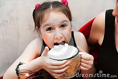 Defocused Funny little Girl Holding Cup with Hot Tasty Chocolate and Marshmellow and trying to eat it on cozy Red Stock Photo