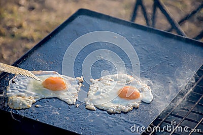 Defocused shot of breakfast camp cooking. Grilling crispy bacon and eggs on a cast iron plate over the camp fire Stock Photo