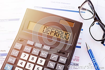 Defraud is a word written on calculator, lying on white surface next to glasses and a blue pen Stock Photo