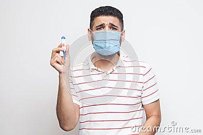 39 degress. Scared panic worry sick man with surgical medical mask standing, holding thermometer are shoched for high temperature Stock Photo