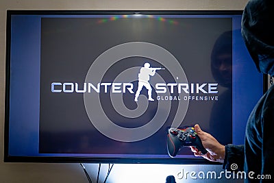 Man holding a steam controller and playing popular video game counter strike on a television and PC Editorial Stock Photo