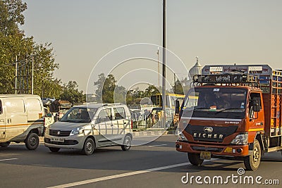 Indian red truck and gray passenger car in city traffic en against the background of green trees and the Editorial Stock Photo