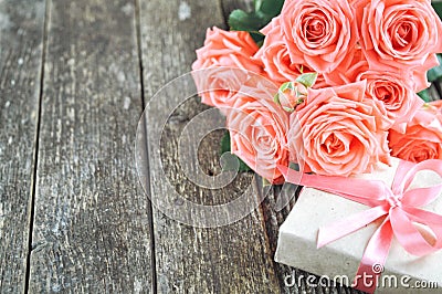 Delicate coral shade pink roses and gift on rustic wooden background. Valentine background. Holiday card for women Stock Photo