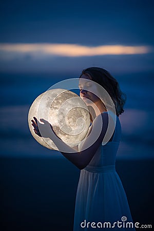 Delicate image of an angel, a girl with the moon in her hands on the night beach. artistic photography. Fairy tale and riddle. Stock Photo