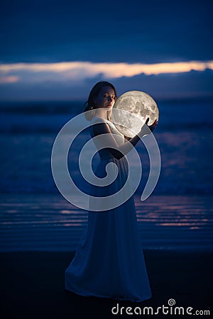 Delicate image of an angel, a girl with the moon in her hands on the night beach. artistic photography. Fairy tale and riddle. Stock Photo