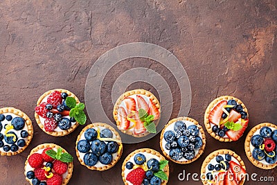 Delicious berry tartlets or cake with cream cheese decorated lemon peel and mint leaf from above. Tasty pastry desserts. Stock Photo