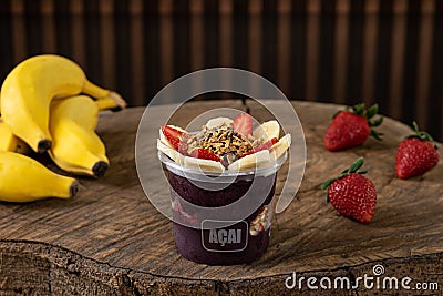 Delicious Brazilian AÃ§aÃ­ Cream, in a plastic Cup With Strawberry, banana and granola Topping, in a rustic wooden background. Editorial Stock Photo