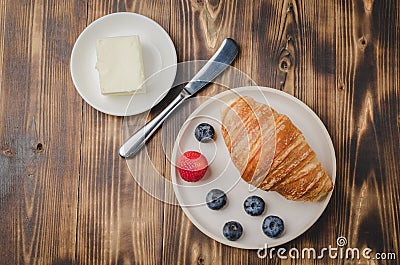 Delicious breakfast with fresh berries.Top view. Croissant with berries in white bowl and butter on wooden background Stock Photo