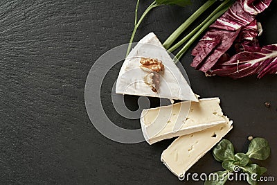 Delicious brie cheese on black background. Brie type of cheese. Camembert. Fresh Brie cheese and a slice on stone board. Italian, Stock Photo