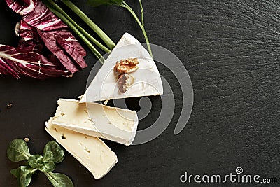 Delicious brie cheese on black background. Brie type of cheese. Camembert. Fresh Brie cheese and a slice on stone board. Italian, Stock Photo