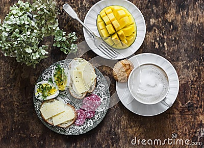 Delicious brunch, breakfast - cappuccino, fresh mango, boiled egg with micro greens, salami, cheese sandwiches on a wooden Stock Photo