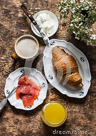 Delicious brunch - cappuccino, croissant, cream cheese, smoked salmon, orange juice on a wooden background, top view Stock Photo