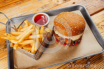 Delicious burger with sauce in a tray with a basket of french fries and ketchup on it Stock Photo