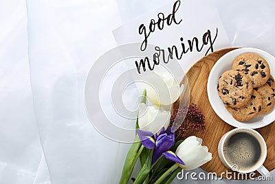 Delicious coffee, cookies, flowers and GOOD MORNING wish on white cloth. Space for text Stock Photo