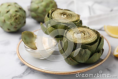 Delicious cooked artichokes with tasty sauce served on white marble table, closeup Stock Photo