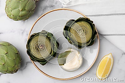 Delicious cooked artichokes with tasty sauce served on white marble table, flat lay Stock Photo