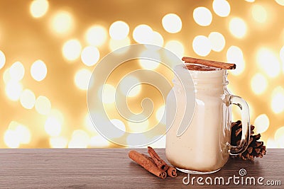Delicious eggnog in mason jar on wooden table against blurred Christmas lights, space for text Stock Photo