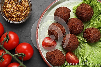 Delicious falafel, tomatoes, lettuce and grain mustard on dark grey textured table, flat lay. Vegan meat products Stock Photo