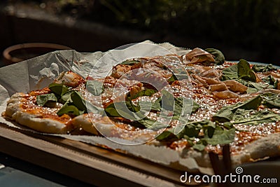 Delicious fresh home made pizza served on a wooden board and some paper. Tasty pizza ready to be cut Stock Photo