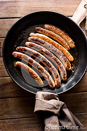 Delicious fried sausages with golden crust in iron cast pan, linen towel, top view Stock Photo