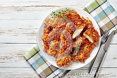 Delicious grated potato coated and deep fried pork chops on a plate on a rustic white wooden table with napkin, fork and knife, Stock Photo