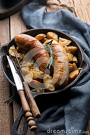 Delicious hot hearty food: fried potatoes with sausages on the grill in a cast iron pan. Stock Photo