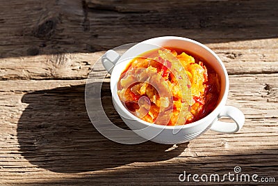 Delicious juicy appetizer of stewed vegetables in white bowl on old wooden table. Rustic style. Sunlight and sharp shadows. Stock Photo