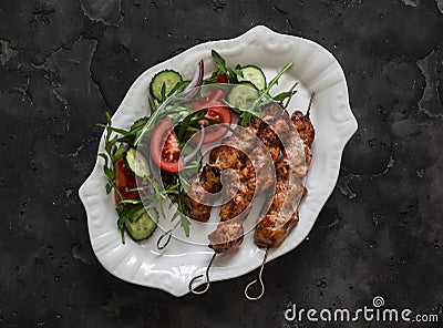 Delicious lunch, appetizer, tapas - chicken skewers and fresh vegetable salad on a dark background, top view Stock Photo