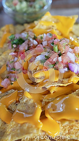 Delicious Mexican cuisine dish, nachos with melted cheddar cheese, roughly chopped tomatoes, onions, peppers and coriander leaves Stock Photo