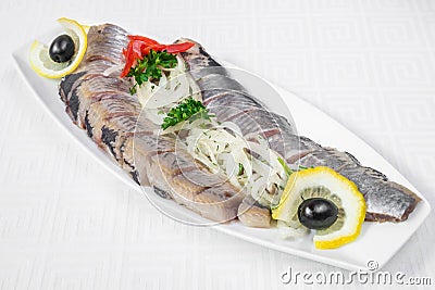 Delicious, mouth-watering slices of sliced herring with onion rings, lemon and herbs, on a white plate. Horizontal frame Stock Photo
