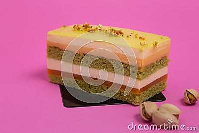 Delicious multi-layer pastry sitting next to a couple of pistachios on a pink background Stock Photo