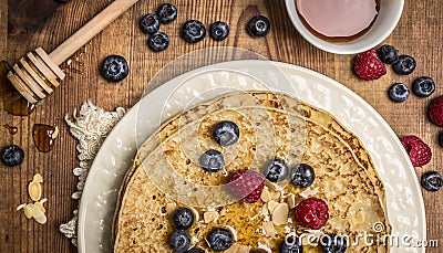 Delicious pancakes with fresh berries with honey, almonds cup of tea with honey spoon on white plate with napkin on wooden rustic Stock Photo