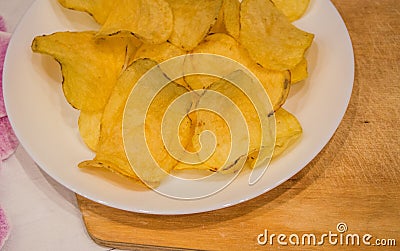 Delicious potato chips round shape, on a white plate on the background of a light wooden table, top view Stock Photo