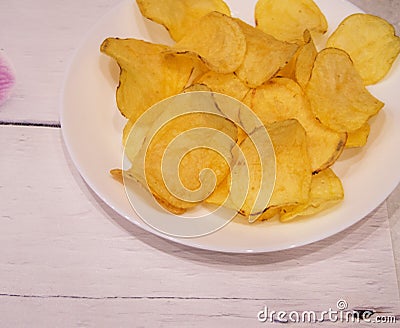 Delicious potato chips round shape, on a white plate on the background of a light wooden table, top view Stock Photo