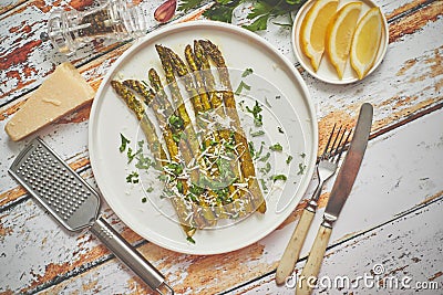 Delicious roasted asparagus served on white ceramic plate. With parmesan cheese, parsley and lemon. Stock Photo