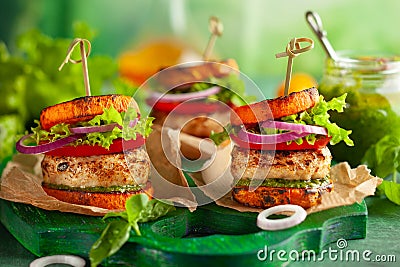 Delicious roasted pumpkin turkey burger with tomatoes and pesto on green wooden board Stock Photo