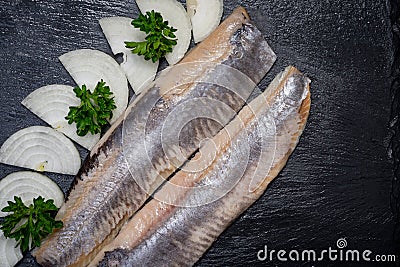 Delicious Salted Herring garnished with Yellow Onion slices and Fresh Parsley. Natural black stone. Clupea harengus. Stock Photo