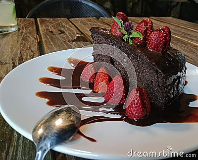 Delicious slice of rich dark chocolate cake with chocolate icing and fresh red strawberries. On wooden table. Stock Photo