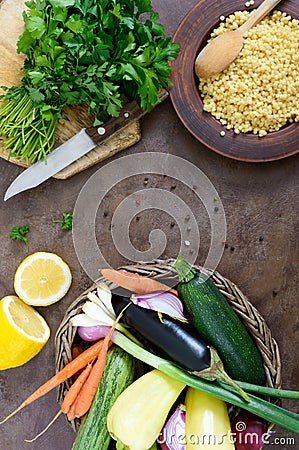 Delicious useful porridge cous cous in a clay plate and raw fresh vegetables in a basket, greens, lemon. Stock Photo