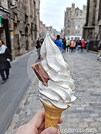 A delicious vanilla Soft serve in waffle cone in a hand Background of blur classic European street. Stock Photo