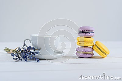 Delicious violet and yellow macarons and cup of latte or americano and branch of fragrant lavender on white wooden Stock Photo