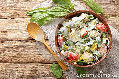 Delicious vitamin salad of boiled eggs, potatoes, tomatoes, onions and sorrel, spinach seasoned with yogurt close-up in a bowl. Stock Photo