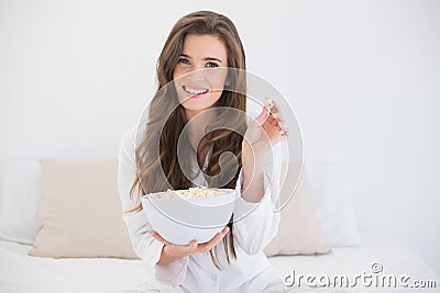 Delighted casual brown haired woman in white pajamas eating popcorn Stock Photo