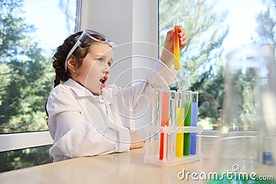 Delighted schoolgirl observes a chemical reaction going in a test tube with colorful reagents and chemicals Stock Photo