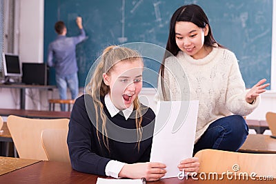 Delighted schoolgirl and Chinese girl schoolmate reading notification Stock Photo
