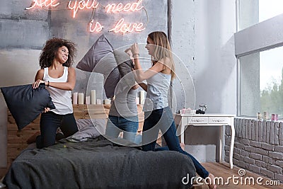 Delighted friends standing on the bed and having pillow fight Stock Photo