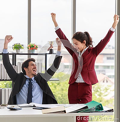 Delighted male and female colleagues smiling and raise hand in air after finishing project in modern office. Teamwork success and Stock Photo
