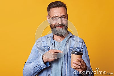 Delighted positive smiling handsome guy holding papercup of strong coffee in one hand, pointing at it with forefinger, having Stock Photo